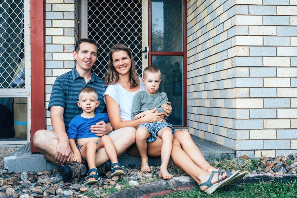 Migrant family with young children sitting in front of a brick house in Australia,