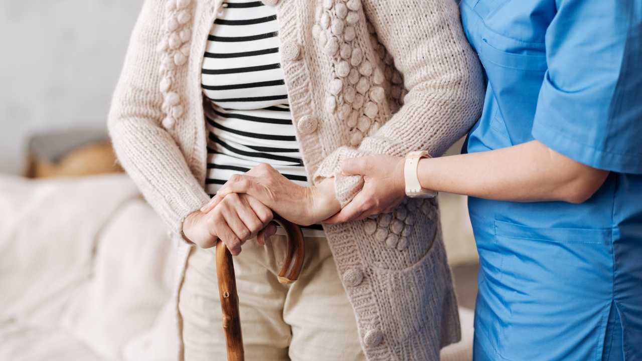 Nurse supporting an older woman with a walking stick in a residential setting, illustrating aged care workforce support in Australia.