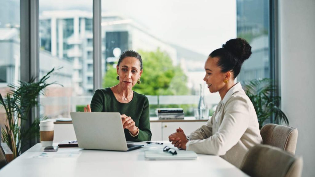 Two HR professionals reviewing a workforce plan on a laptop during a meeting.