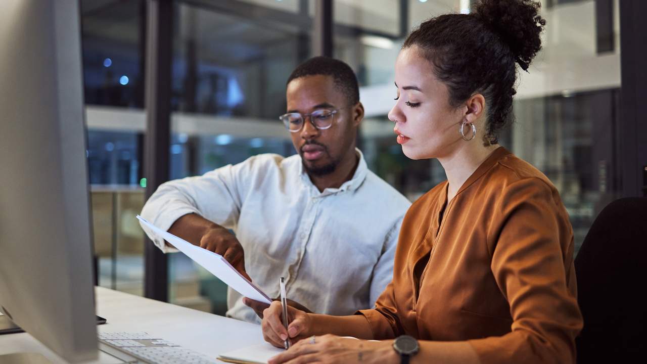 Two professionals reviewing documents at a desk in an office, discussing salary and sponsorship matters.