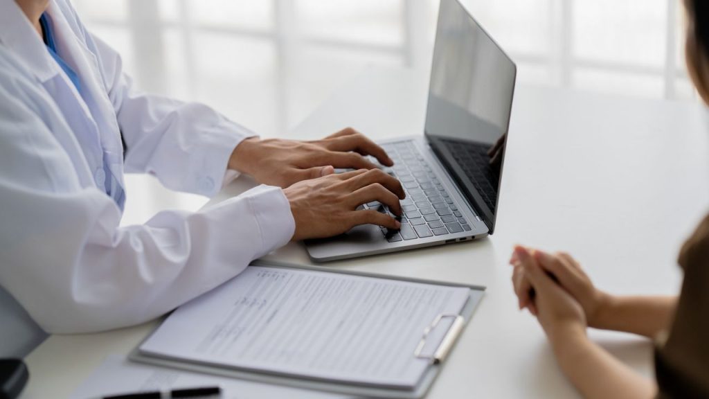 Doctor typing on a laptop during a hospital consultation, representing medical workforce retention and permanent residency support.